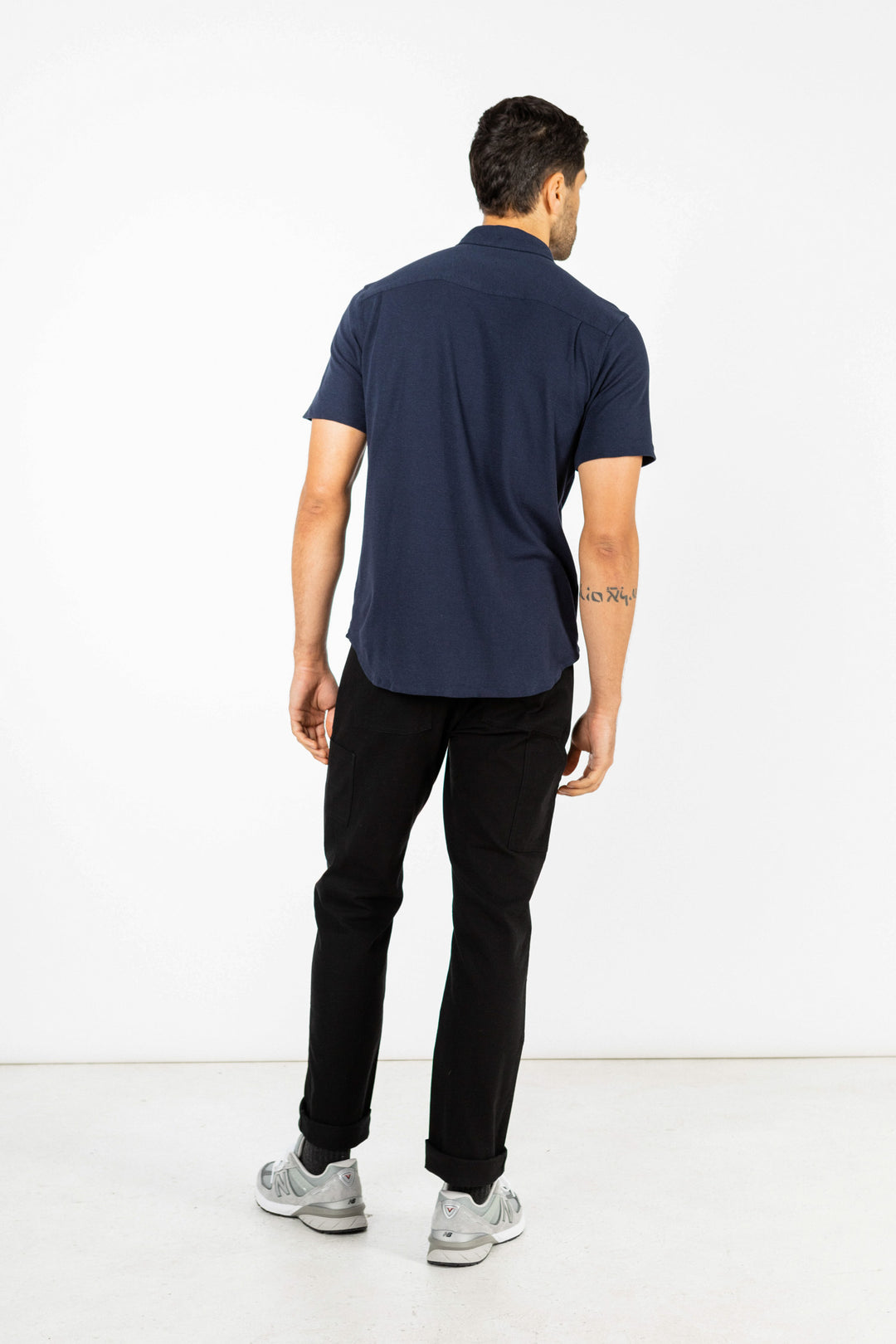 A man faces away from the camera, wearing the Bridge & Burn Gary Knit Pullover in navy jersey and black pants, with gray sneakers, set against a plain white background.