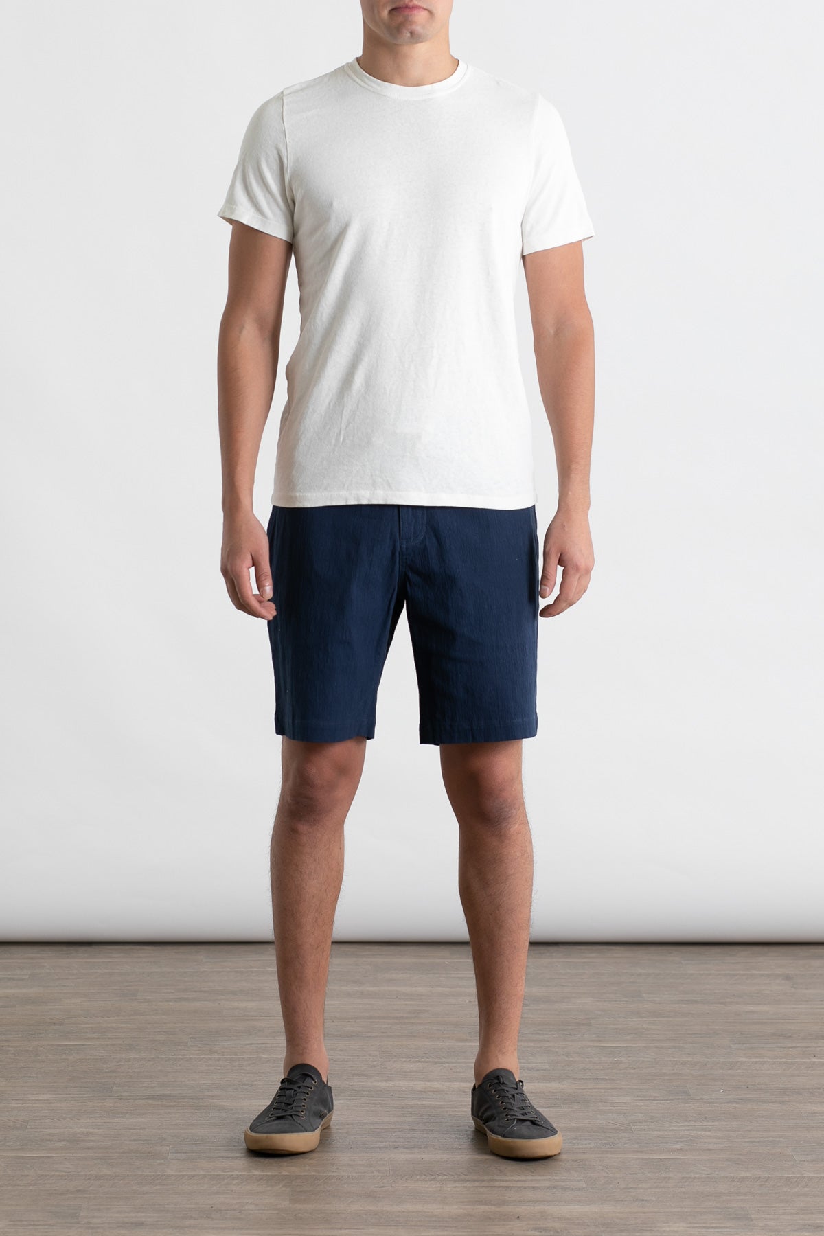 A man stands indoors against a plain white background, wearing the Jungmaven Baja Tee in Washed White. His arms are at his sides and his face is not visible.
