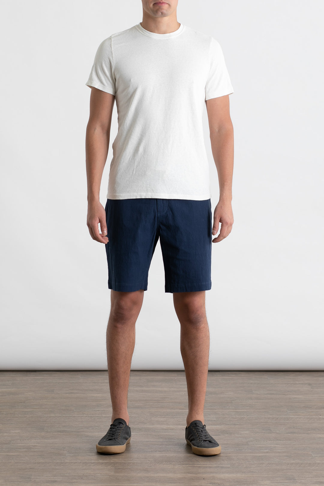 A man stands indoors against a plain white background, wearing the Jungmaven Baja Tee in Washed White. His arms are at his sides and his face is not visible.