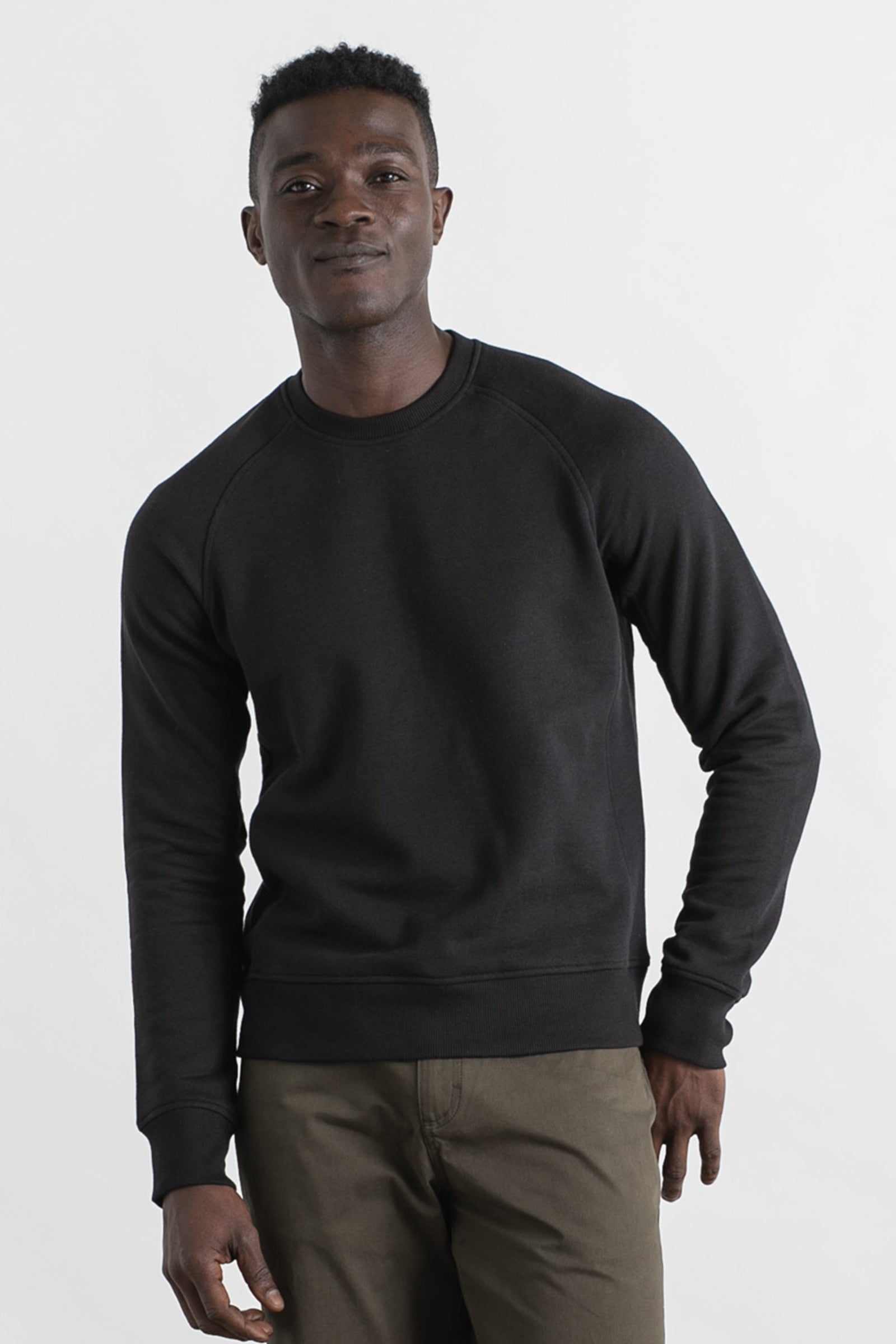 A man faces the camera wearing the Bridge & Burn Fremont Crew Sweatshirt in black with olive green pants, set against a plain white background.