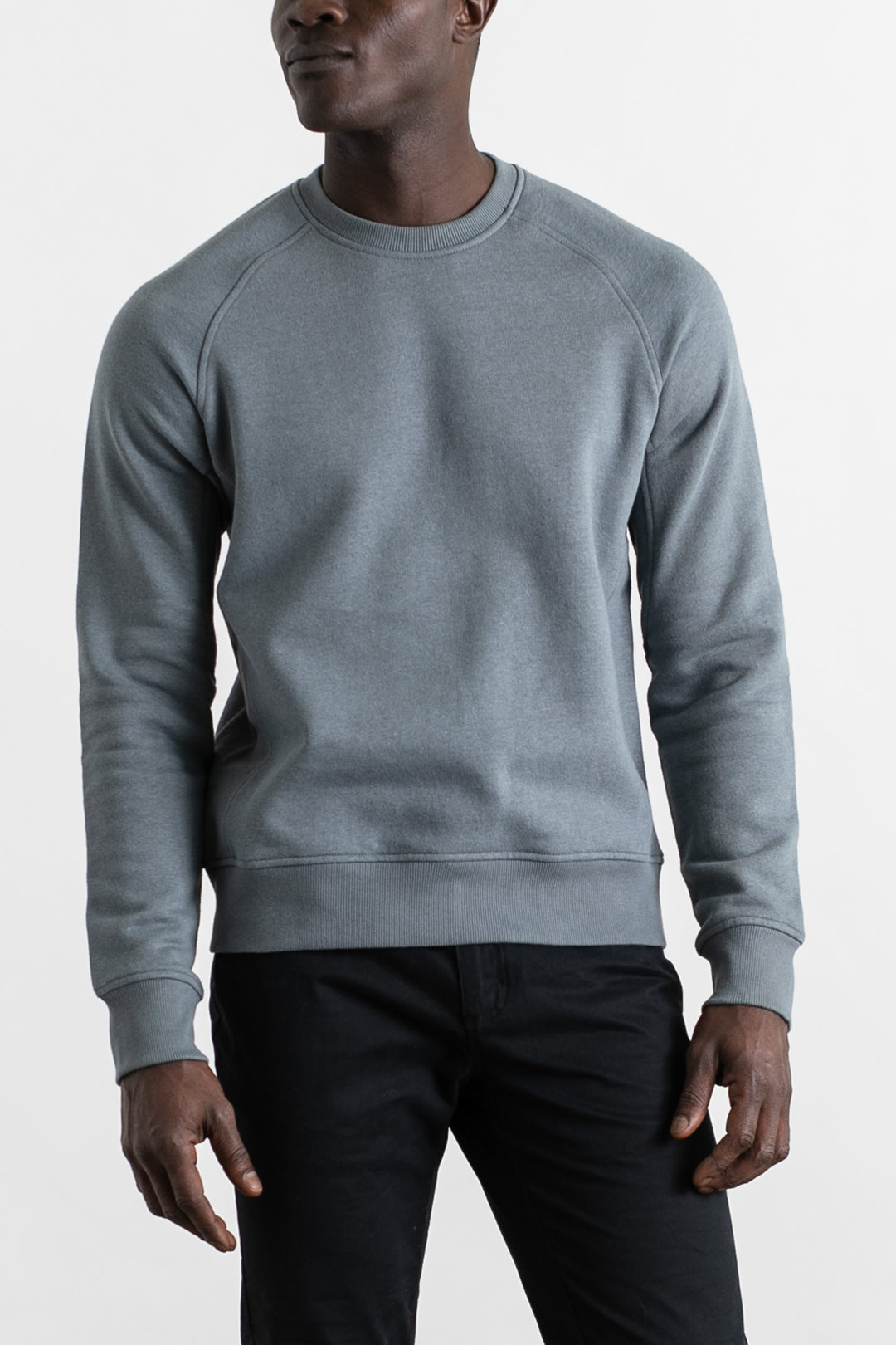 A person wears a Bridge & Burn Fremont Crew Sweatshirt in Storm Blue and black pants, standing against a plain white background with arms relaxed at their sides.