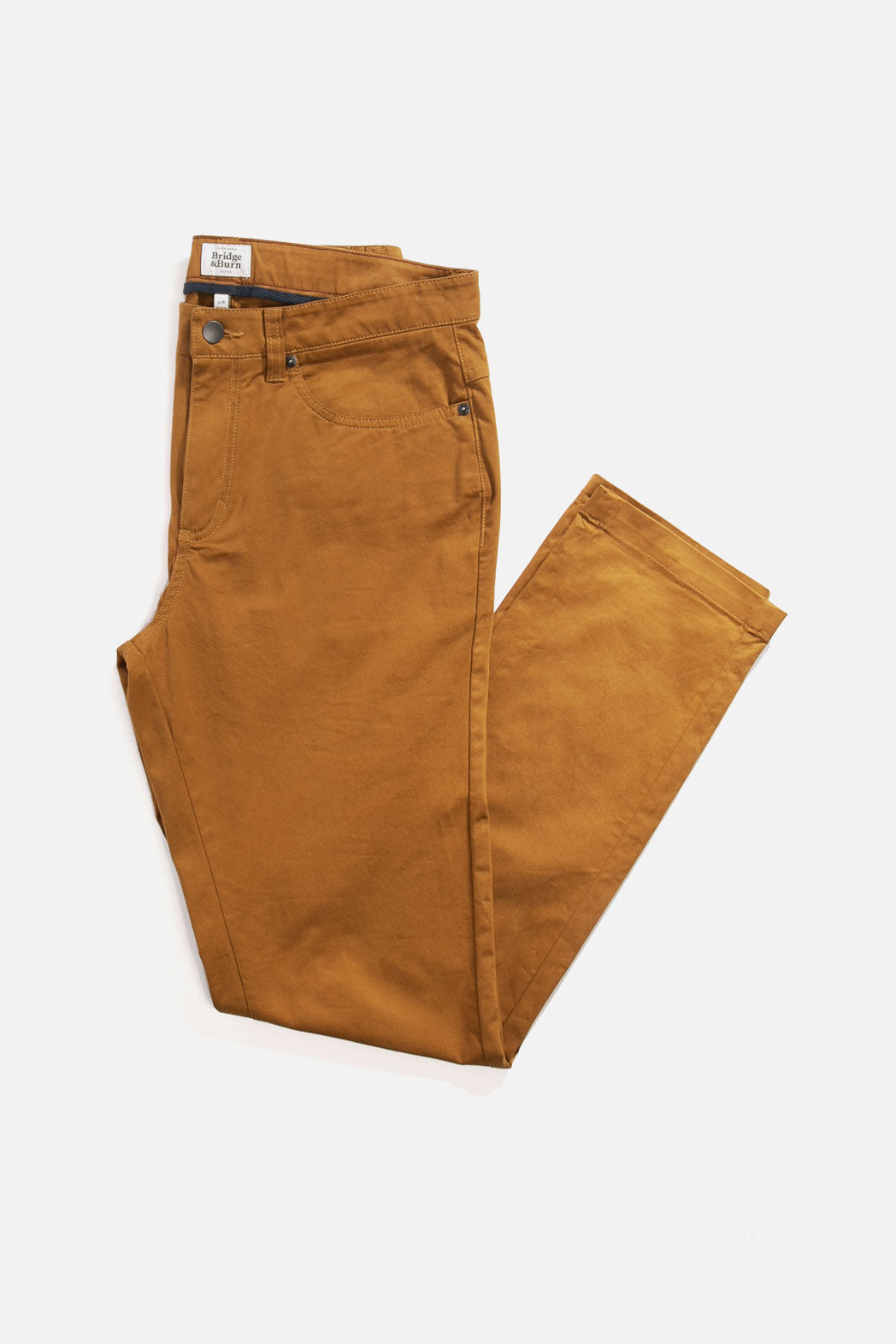 The Bridge & Burn Bradley Slim Pant in Flax, featuring a classic 5-pocket design and slim fit, is shown neatly folded against a white background.