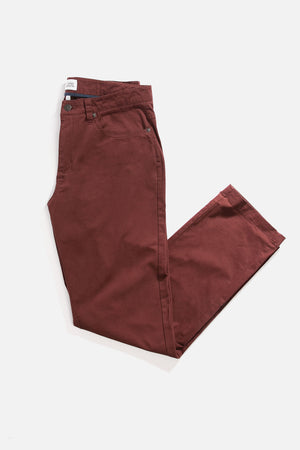 The Polk Pant in burgundy by Bridge & Burn, a pair of straight-fit pants with a front pocket and visible brand tag on the waistband, is neatly folded on a white background.