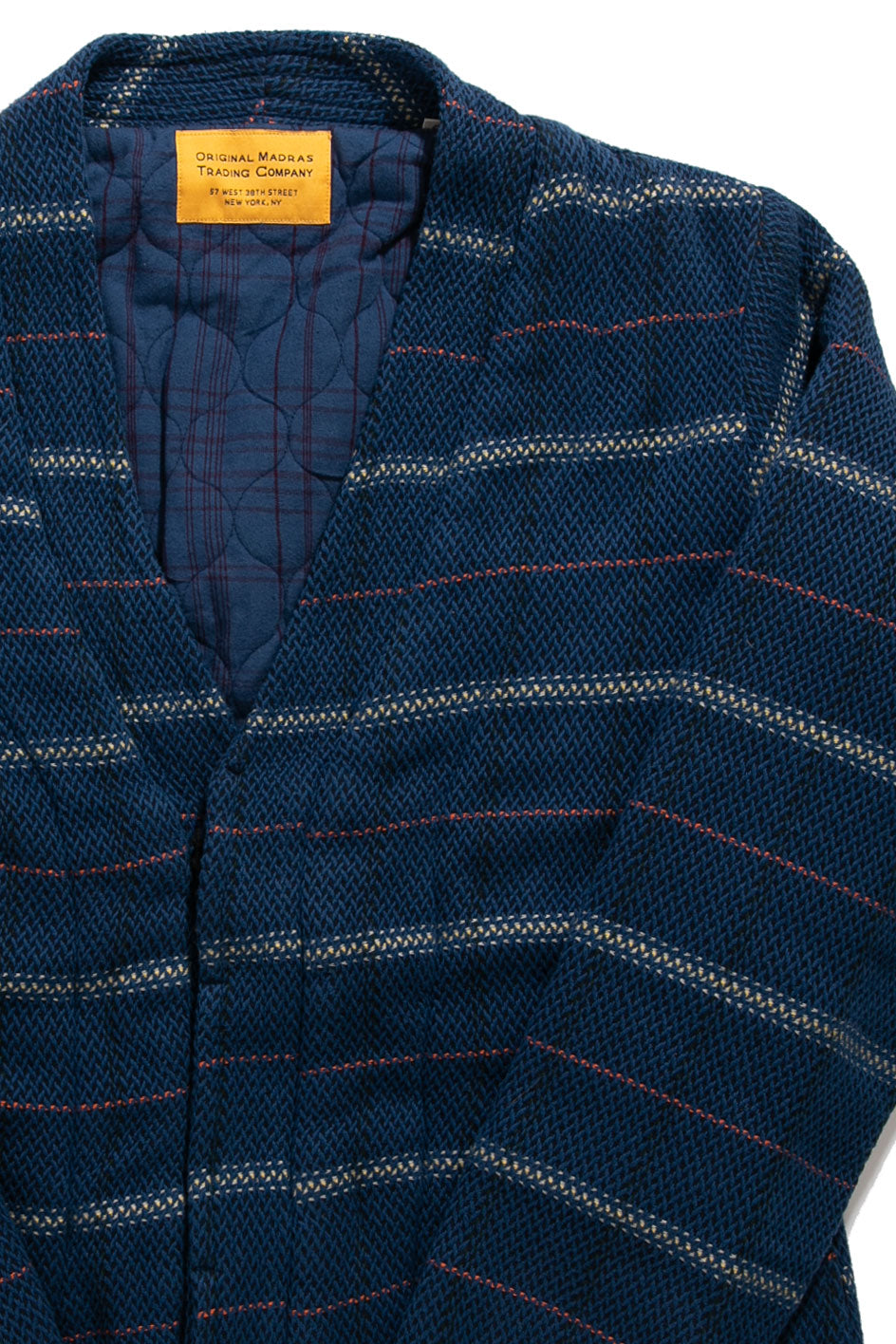 A close-up of the Original Madras Trading Company Chevron Weave Lined Cardigan, a blue quilted jacket with red and white stripes, tan branded label at the collar, and a soft quilted lining for extra warmth.